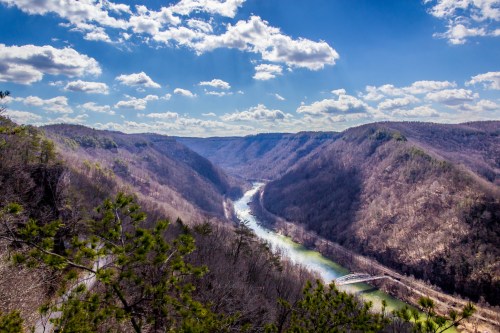 A scenic view of a winding river surrounded by mountains under a blue sky with fluffy clouds.