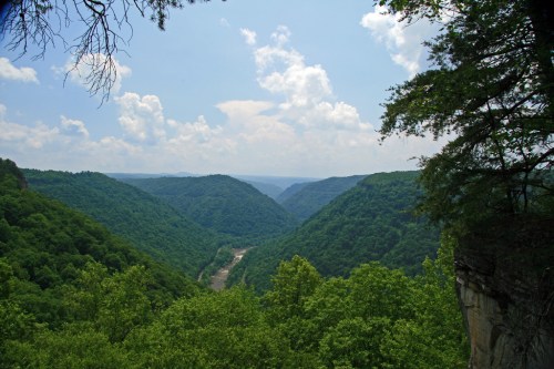 A scenic view of a lush green valley with a river winding through, under a partly cloudy sky.