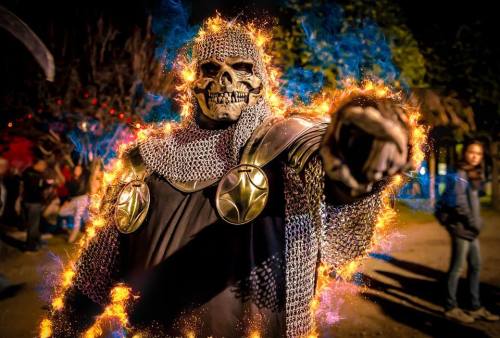 A skeleton in chainmail armor surrounded by flames, posing dramatically at a nighttime event.