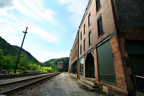 A view of a brick building alongside a railway track, with green hills in the background under a blue sky.