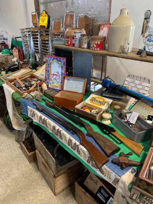 A display of vintage items, including rifles, tools, and various collectibles on a table with wooden crates.