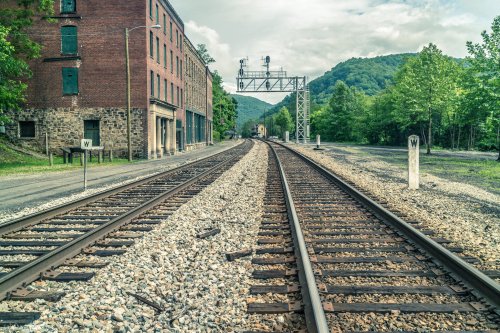 A view of railway tracks curving through a rural area, with an old brick building and green hills in the background.