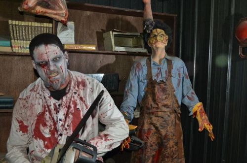 Two gruesome, bloodied figures in a dimly lit room, one holding a chainsaw and the other with a menacing pose.