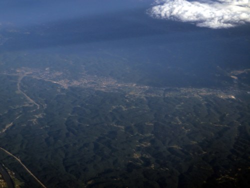 Aerial view of a mountainous landscape with valleys and a small town visible beneath a cloudy sky.