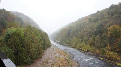 A misty river flows between lush, green hills, creating a serene and tranquil landscape.