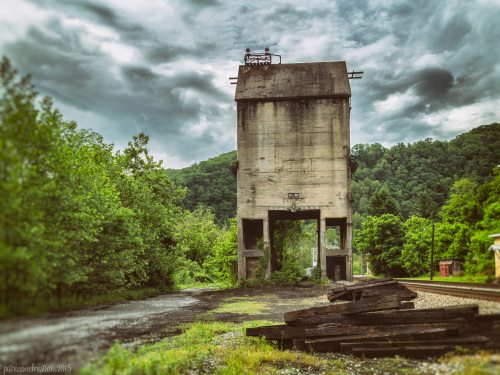 Abandoned concrete structure surrounded by greenery under a cloudy sky, with old wooden beams in the foreground.