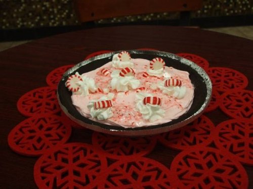 A festive pie with pink filling, topped with whipped cream and peppermint candies, on a red snowflake table mat.