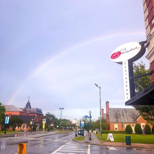 A rainbow arcs over a street scene featuring a restaurant sign and wet pavement after rain.