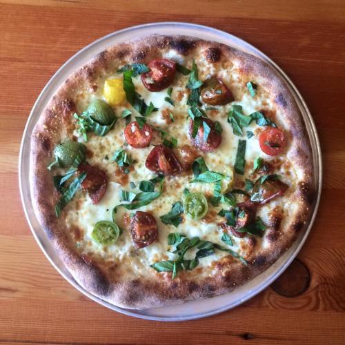 A freshly baked pizza topped with sliced tomatoes and fresh basil on a wooden table.