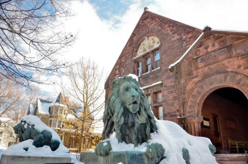 A snow-covered lion statue stands in front of a historic stone building with intricate architectural details.