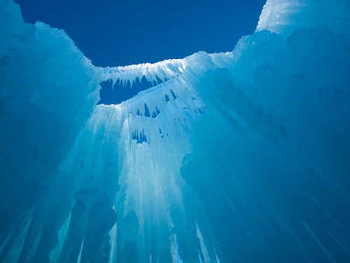 A stunning view of icy blue formations hanging from above, creating a natural ice cave against a clear blue sky.