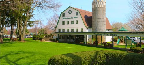 A charming white building with a tower, surrounded by green grass and trees, housing shops and gifts.