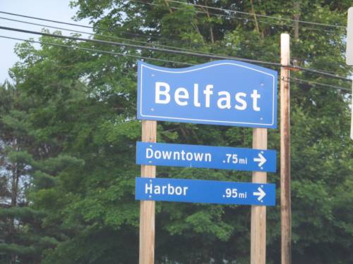 Sign for Belfast with directions to Downtown (0.75 miles) and Harbor (0.95 miles), surrounded by greenery.
