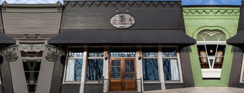 A row of storefronts featuring a mix of architectural styles and colors, with large windows and awnings.