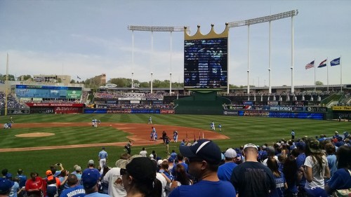 A baseball stadium filled with fans, featuring players on the field and a large scoreboard in the background.