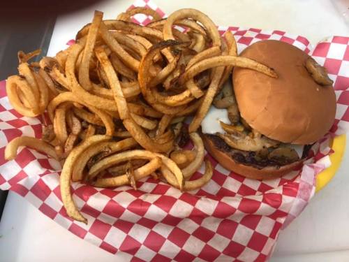 A burger with melted cheese and grilled onions served with a large portion of curly fries in a red and white checkered basket.