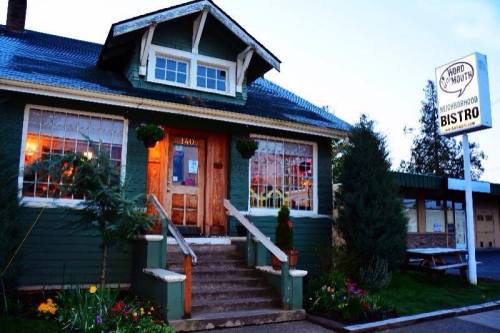A charming green bistro with a welcoming entrance, surrounded by flowers and trees, under a twilight sky.