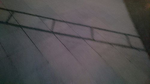 A shadow of a ladder cast on a textured surface, creating an abstract pattern in dim lighting.