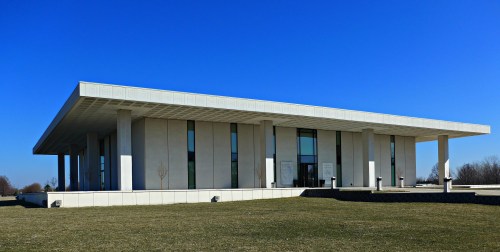 A modern, minimalist building with a flat roof and large glass windows, set against a clear blue sky.