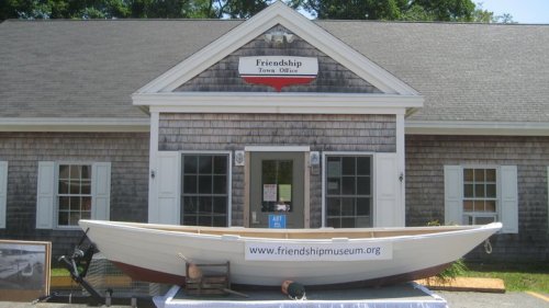 A white boat displayed in front of the Friendship Town Office, featuring a sign for the Friendship Museum.