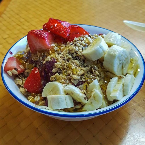 A bowl of acai topped with sliced bananas, strawberries, granola, and a drizzle of honey.