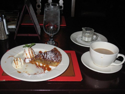 A plate with dessert, including a slice of pie, ice cream, and sauce, alongside a cup of coffee and a glass of water.