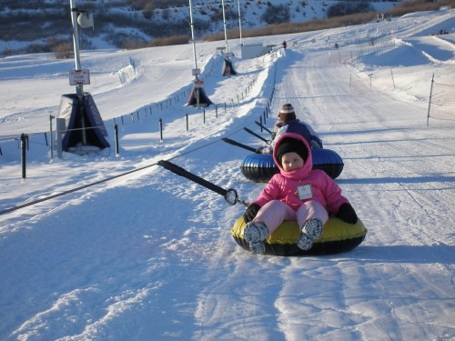 Children in colorful snow tubes slide down a snowy hill on a winter day.