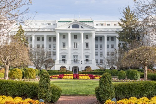 A grand white building with a classic facade, surrounded by colorful flower beds and manicured gardens.
