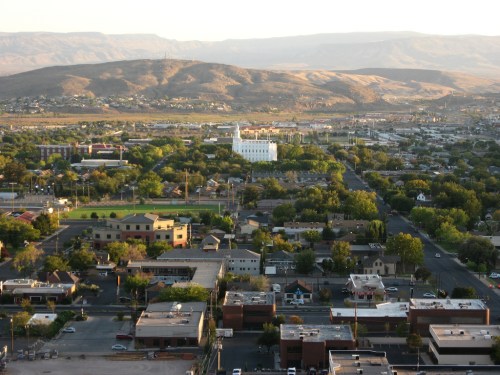 Aerial view of a city with green parks, buildings, and mountains in the background under a clear sky.