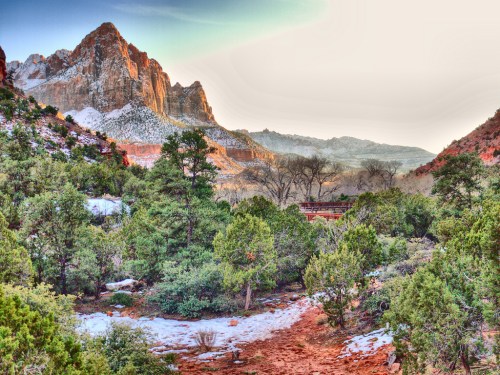 A scenic view of snow-dusted mountains surrounded by lush greenery and a winding path in a tranquil landscape.