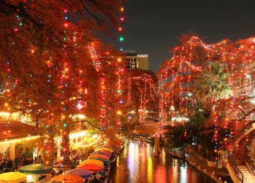 A vibrant night scene of a river lined with colorful lights and trees, reflecting on the water's surface.