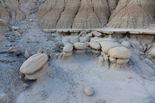 Barren landscape featuring unique, rounded rock formations amidst dry, cracked earth and scattered stones.