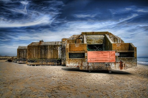 A weathered, abandoned structure on a beach, with a "Keep Off" sign and dramatic clouds in the background.