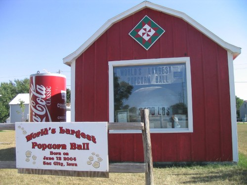 Red building with a sign for the "World's Largest Popcorn Ball" and a large Coca-Cola can nearby.
