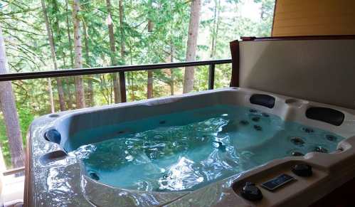 A hot tub with bubbling water, set on a balcony surrounded by tall trees and greenery.