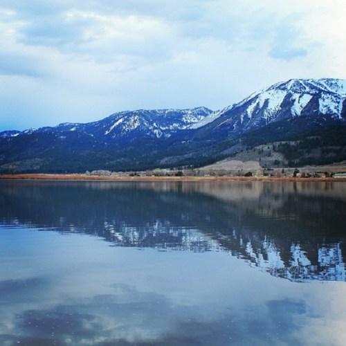 A serene landscape featuring snow-capped mountains reflected in a calm lake under a blue sky.