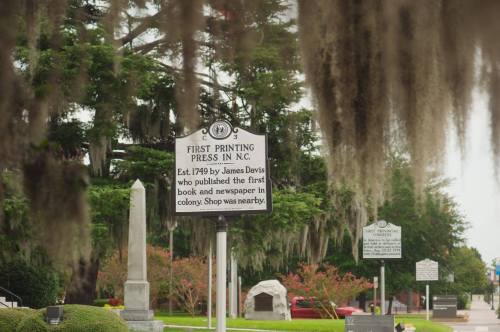 Historic marker for the first printing press in North Carolina, established in 1749 by James Davis, with trees in the background.