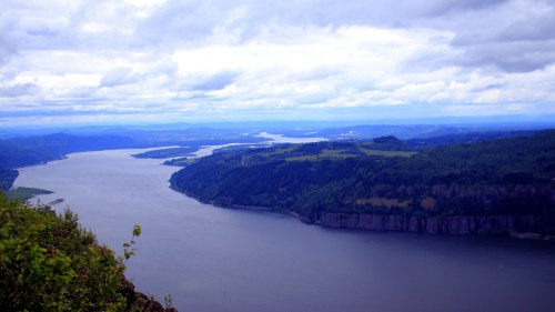 A scenic view of a river winding through lush green hills under a cloudy sky.