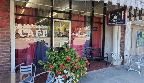 A cozy café and bookstore with a welcoming entrance, featuring red curtains and a flower arrangement outside.