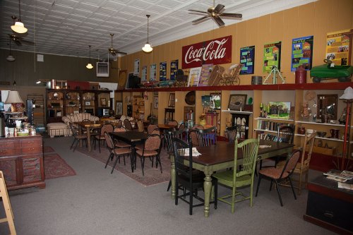A cozy vintage shop interior with wooden tables, chairs, and shelves displaying various antiques and decor.