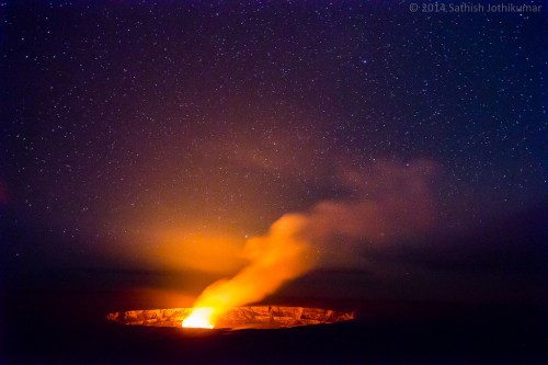 A glowing volcano emits smoke against a starry night sky, creating a dramatic contrast of light and darkness.