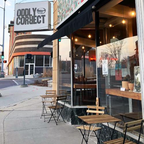 Exterior of "Oddly Correct" café with outdoor seating and a sign, located on a city street at dusk.