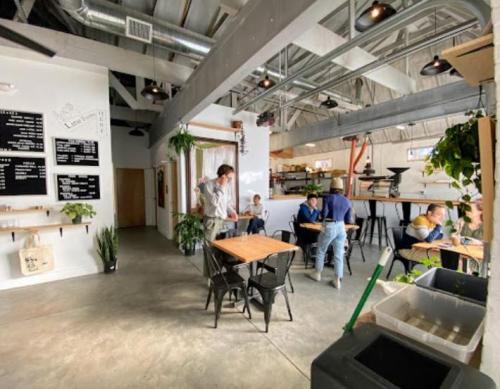 A modern café interior with tables, plants, and people dining and working. Bright, open space with industrial decor.