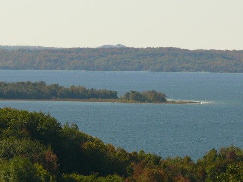 A serene view of a lake surrounded by lush greenery and distant hills under a clear sky.
