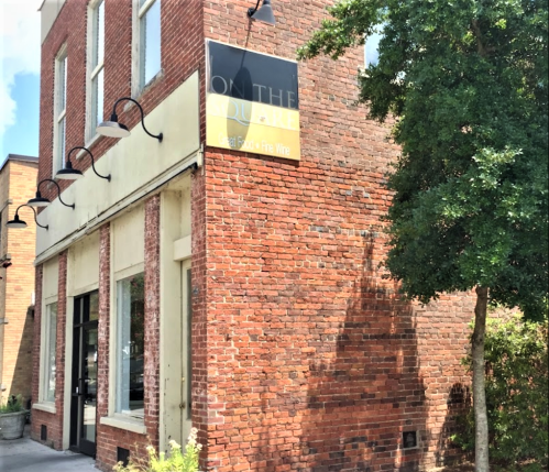 A brick building with a sign reading "On the Square" and greenery nearby.