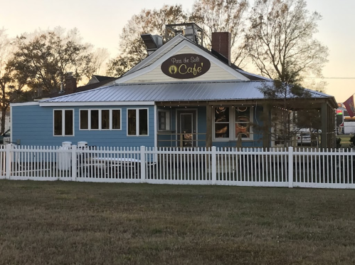A blue café building with a white picket fence and a sign that reads "Pass the Salt Café." Trees in the background.