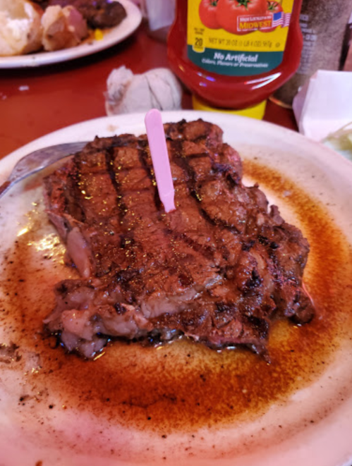 A grilled steak on a plate with a pink marker, surrounded by sauce and condiments in the background.