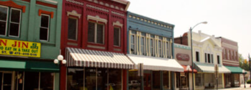Colorful storefronts with awnings line a quaint street, showcasing a charming small-town atmosphere.