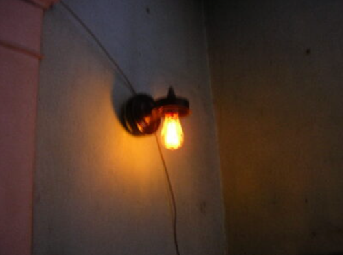 A vintage-style light bulb emits a warm glow, mounted on a wall with a simple black fixture.