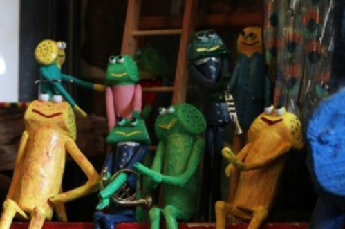 Colorful wooden frog figurines in various poses, some playing instruments, in a whimsical display.